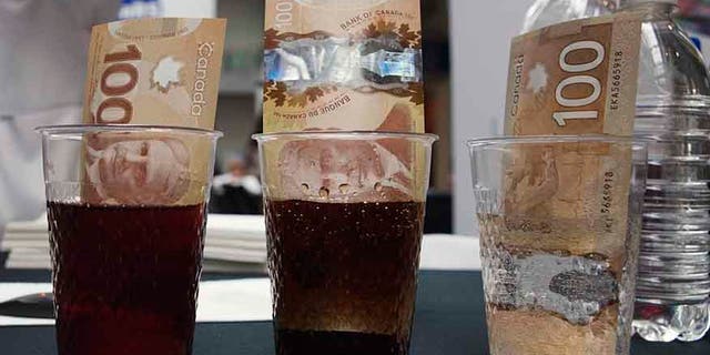 Canadian 100 dollar bills made of polymer are placed in glasses of juice, cola and water.