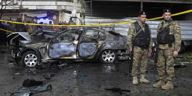 Officials stand in front of a car that was destroyed in a bombing in the southern port city of Sidon, Lebanon, Sunday, Jan. 14, 2018