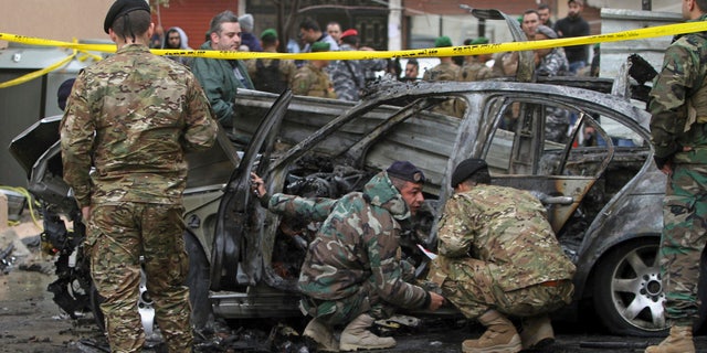 Officials examine a car that was destroyed in a bombing in the southern port city of Sidon, Lebanon, Sunday, Jan. 14, 2018