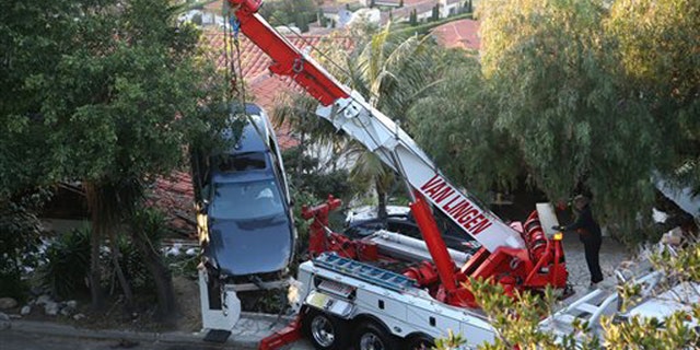 A crane removes a car that crashed off Palos Verdes Drive west and ended up on the roof of a home in Palos Verdes Estates, Calif. Wednesday, Feb. 3, 2016. Firefighters pulled the man from the damaged car and took him to a hospital, but he wasnt seriously hurt, and no one else was injured. (Chuck Bennett/Daily Breeze via AP)