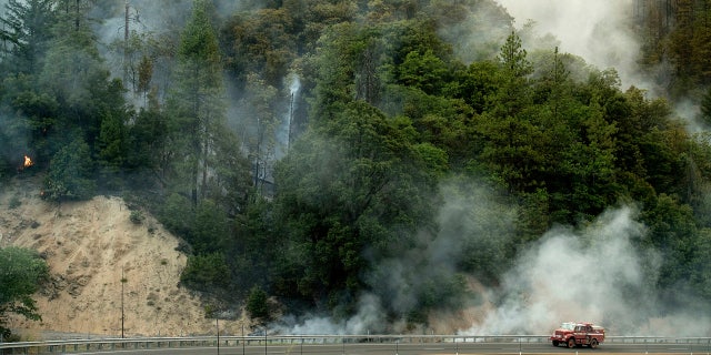 A fire truck passes a smoldering hillside as the Carr Fire burns along Highway 299 in unincorporated Shasta County, Calif.