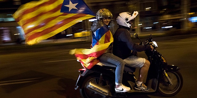 A woman holds a Catalan independence flag on a motorcycle after taking part in a protest against the National Court's decision to jail civil society leaders without bail in Barcelona, Spain.