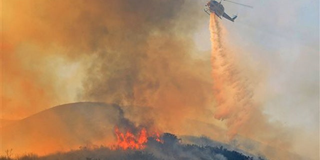 A Ventura County Fire helicopter makes a water drop on an oil field service road while working a wildfire in Ventura County, Calif. on Saturday, Dec. 26, 2015. (Mike Eliason/Santa Barbara County Fire Dept. via AP)
