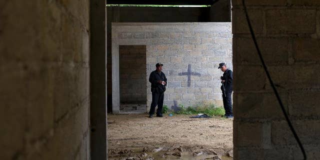 FILE - In this Thursday, July 3, 2014, file photo, state police stand inside a warehouse where a black cross covers a wall near blood stains on the ground, after a shootout between Mexican soldiers and alleged criminals on the outskirts of the village of San Pedro Limon, in Mexico state, Mexico. Mexico's Defense Department said Thursday Sept. 25  2014, that an army officer and seven soldiers have been detained in connection with the killing of 22 people in the rural town in southern Mexico. (AP Photo/Rebecca Blackwell, File)