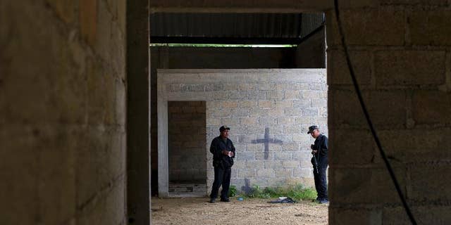FILE - In this Thursday, July 3, 2014, file photo, state police stand inside a warehouse where a black cross covers a wall near blood stains on the ground, after a shootout between Mexican soldiers and alleged criminals on the outskirts of the village of San Pedro Limon, in Mexico state, Mexico. Mexico's Defense Department said Thursday Sept. 25 2014, that an army officer and seven soldiers have been detained in connection with the killing of 22 people in the rural town in southern Mexico. (AP Photo/Rebecca Blackwell, File)