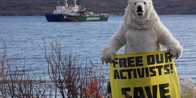 An activist dressed as a polar bear holds a banner in front of Greenpeace's Arctic protest ship, moored beside a Russian Coast Guard ship in Kola Bay near Murmansk on September 24, 2013, in a photo provided by Greenpeace International