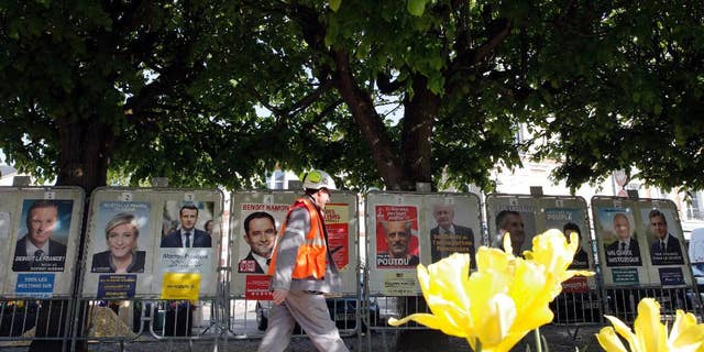 A man walks past French presidential campaign posters displayed in Marnes-la-Coquette, outside Paris, Thursday, April 20, 2017. The two-round presidential election is set for April 23 and May 7. (AP Photo/Christophe Ena)
