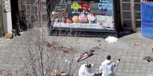 Two men in haz-mat suits investigate the scene of the first bombing on Boylston Street in Boston Tuesday, April 16, 2013 near the finish line of the 2013 Boston Marathon, a day after two blasts nearby killed three and injured over 170 people. (AP Photo/Elise Amendola)