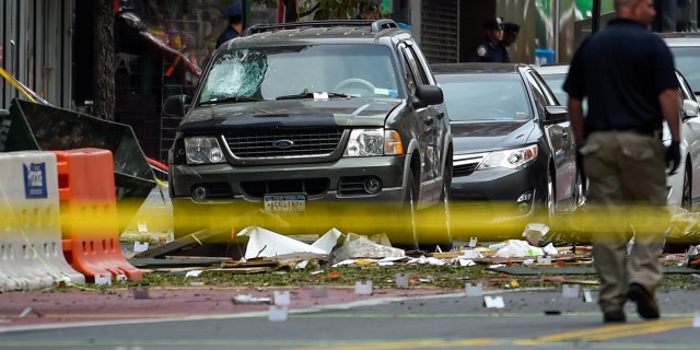 A vehicle is left damaged next to a garbage dumpster as a security official walks past the site of an explosion in the Chelsea neighborhood of Manhattan, New York, U.S. September 18, 2016.