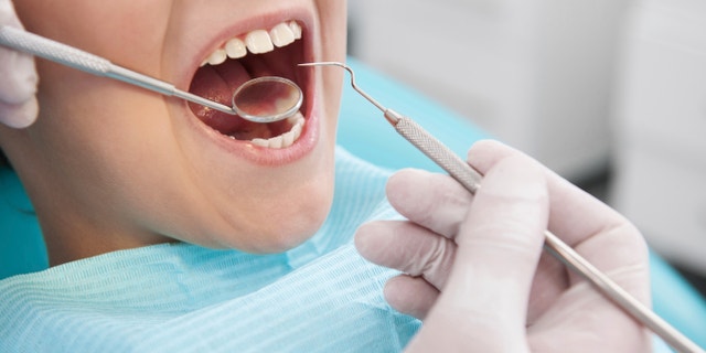 Little boy sitting at the chair at the dental office while doctor examining teeth
