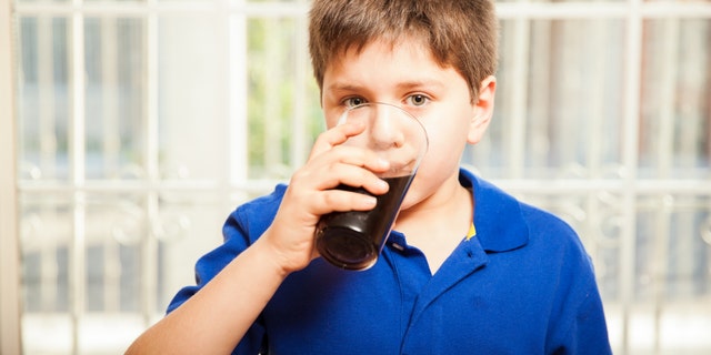 Portrait of a young boy drinking soda from a glass at home
