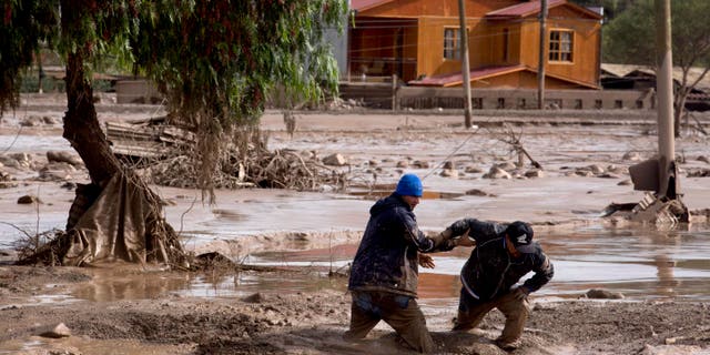 Dos hombres se ayudan entre sà a cruzar una calle cubierta en lodo en Copiapó, Chile, el jueves 26 de marzo de 2015. Inusuales tormentas y lluvias torrenciales que comenzaron el martes, han bloqueado los caminos, provocado fallas eléctricas y afectado a unas 600 personas en esta región habitualmente seca. (Foto AP/Pablo Sanhueza)