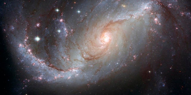 This photo supplied by NASA and the European Space Agency Tuesday, April 3, 2007, is a Hubble Space Telescope view of the barred spiral galaxy NGC 1672, showing up clusters of hot young blue stars along its spiral arms, and clouds of hydrogen gas glowing in red. Delicate curtains of dust partially obscure and redden the light of the stars behind them. NGC 1672s symmetric look is emphasized by the four principal arms, edged by eye-catching dust lanes that extend out from the center. The galaxy, visible from the Southern Hemisphere, is seen almost face on and shows regions of intense star formation. The greatest concentrations of star formation are found in the so-called starburst regions near the ends of the galaxys strong galactic bar. (AP Photo/NASA-ESA) Credit: NASA, ESA