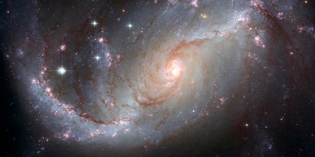 This photo supplied by NASA and the European Space Agency Tuesday, April 3, 2007, is a Hubble Space Telescope view of the barred spiral galaxy NGC 1672, showing up clusters of hot young blue stars along its spiral arms, and clouds of hydrogen gas glowing in red. Delicate curtains of dust partially obscure and redden the light of the stars behind them. NGC 1672s symmetric look is emphasized by the four principal arms, edged by eye-catching dust lanes that extend out from the center. The galaxy, visible from the Southern Hemisphere, is seen almost face on and shows regions of intense star formation. The greatest concentrations of star formation are found in the so-called starburst regions near the ends of the galaxys strong galactic bar. (AP Photo/NASA-ESA) Credit: NASA, ESA