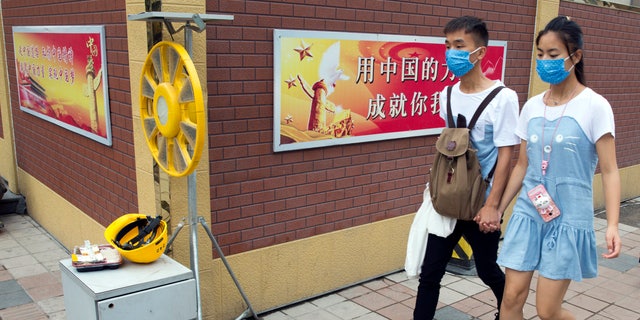 In this Friday, July 15, 2016 photo, a Chinese couple wearing masks to protect against air pollution walk past a Chinese government propaganda slogan for the "Chinese Dream" in Beijing. Beijing's notoriously awful air quality improved significantly in the first half of the year, with actions taken to curb the city's heavy pollution having a positive effect, officials in the Chinese capital said Monday, July 19, 2016. (AP Photo/Ng Han Guan)