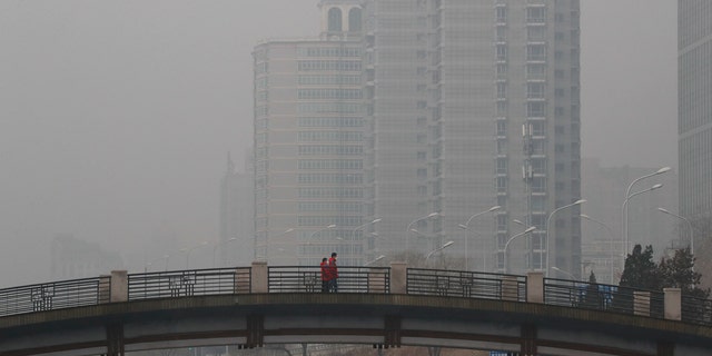 Chinese men wearing masks to filter the pollution walk on a bridge near building shrouded by fog and pollution in Beijing, Thursday, Jan. 5, 2017.