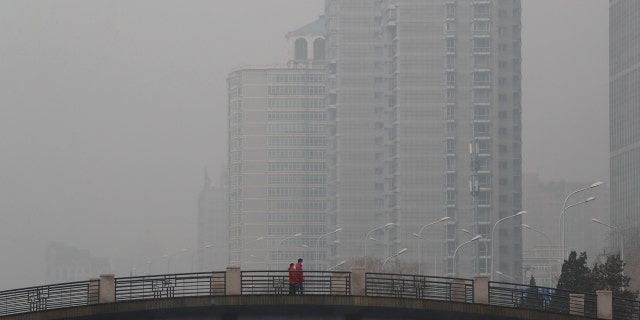Chinese men wearing masks to filter the pollution walk on a bridge near building shrouded by fog and pollution in Beijing, Thursday, Jan. 5, 2017.