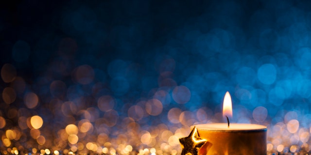Tea light and a golden star on defocused blue and gold background.
