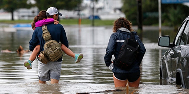 Don Noel carries his daughter Alexis with his wife Lauren as they walk through a flooded roadway to check on their boat in the West End section of New Orleans, June 21.