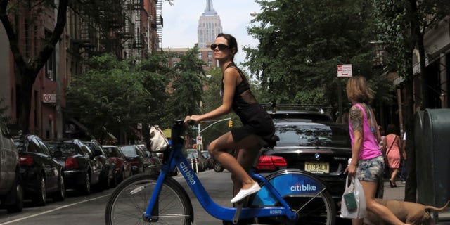 The Empire State Building is seen in the distance as a woman rides a Citibike in the Soho neighbourhood of New York July 27, 2013. REUTERS/Gary Hershorn