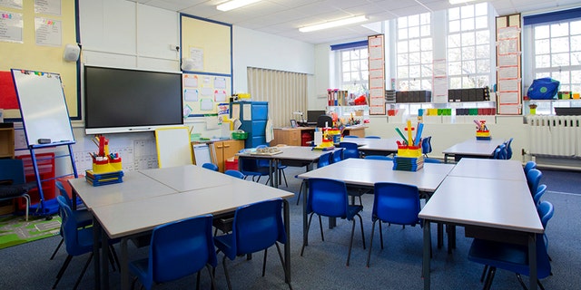 A horizontal image of an empty primary school classroom. The setting is typically British.