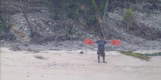 One of three castaways discovered by a U.S. Navy P-8A aircraft waves lifejackets to attract attention on the uninhabited island of Fanadik. (U.S. Navy photo)