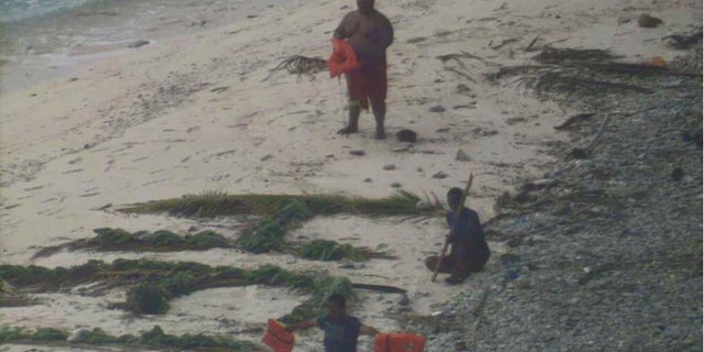 Three men wave life jackets and look on as a U.S. Navy P-8A Poseidon maritime surveillance aircraft discovers them on the uninhabited island of Fanadik. (U.S. Navy photo)