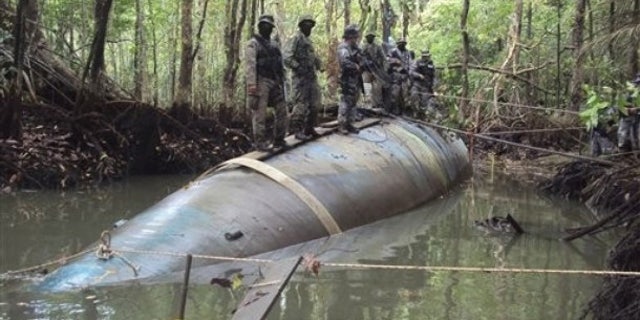 Soldiers stand on a seized submarine in the jungle region of La Loma in Ecuador, Saturday July 3, 2010. DEA officials said that the diesel electric-powered submarine was constructed in a remote jungle and captured near a tributary close to the Ecuador-Colombia border and is capable of transporting tons of cocaine.