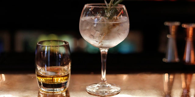 A Gin Cocktail and glass of whisky sit side by side on a bar.