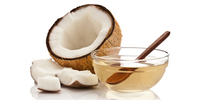 Glass bowl filled with coconut oil and half coconut with pieces isolated on white background