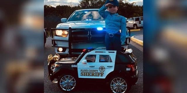 Three-year-old Cohen standing at attention in his electric toy police car.