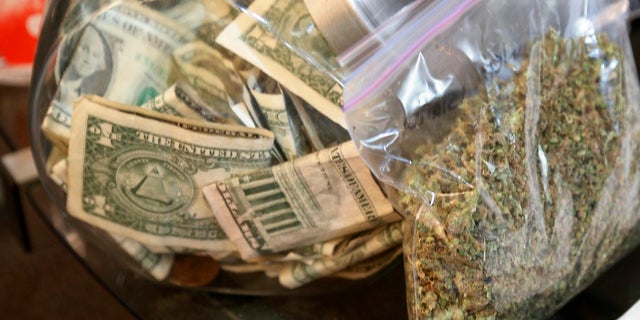 A bag of marijuana being prepared for sale sits next to a money jar at BotanaCare in Northglenn, Colorado.