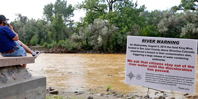 Aug. 8, 2015: A warning sign from the city is displayed in front of the Animas River as orange sludge from a mine spill upstream flows past Berg Park in Farmington, N.M.