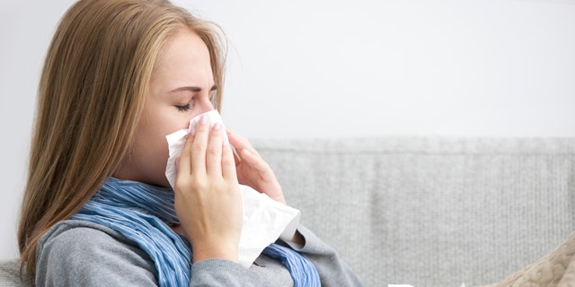 Close up of a young woman sneezing into a tissue. 