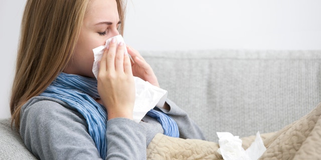 Close up of a young woman sneezing into a tissue.