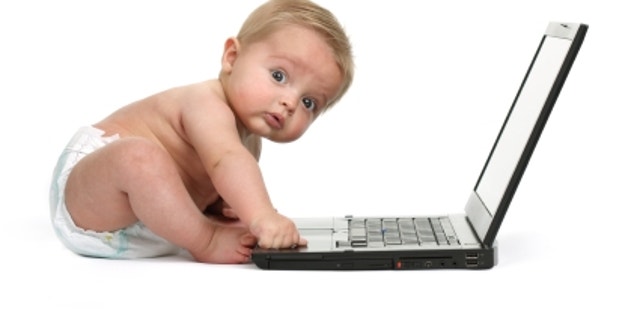 Surprised expression on a baby boys face whilst getting into mischief on a laptop computer