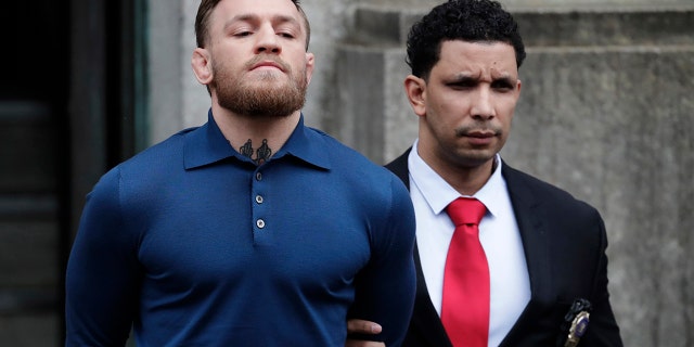 Ultimate fighting star Conor McGregor, left, is led by an official to an unmarked vehicle while leaving the 78th Precinct of the New York Police Department, Friday, April 6, 2018, in the Brooklyn borough of New York. McGregor is facing criminal charges in the wake of a backstage melee he allegedly instigated that has forced the removal of three fights from UFC's biggest card of the year. Video footage appears to show the promotion's most bankable star throwing a hand truck at a bus full of fighters after a Thursday news conference for UFC 223 at Brooklyn's Barclays Center. (AP Photo/Julio Cortez)
