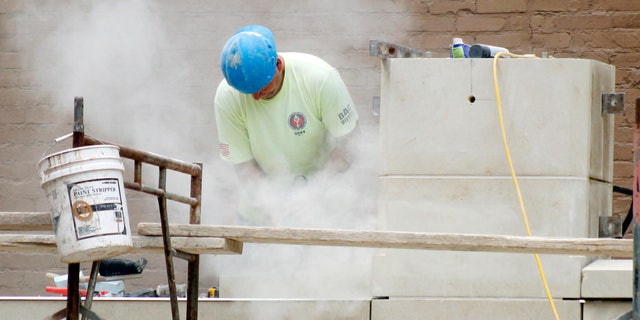 In this July 21, 2011 photo, a workman stands in a cloud of dust as he grinds block for fitment at a construction site at Point Park College in downtown Pittsburgh.