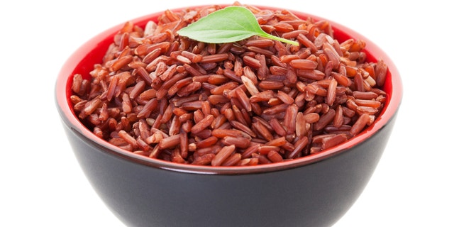 A bowl of Red Cargo Rice garnished with a single leaf of lemon basil. Shot on white background.