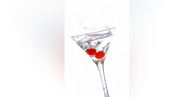 Two red cherrys splashing into a cocktail glass