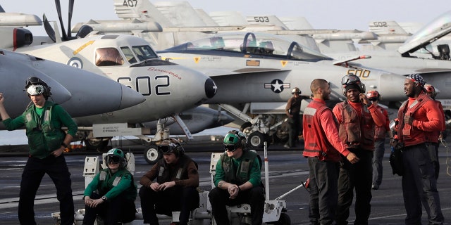 U.S. Navy sailors stand on the deck of the U.S.S. Dwight D. Eisenhower aircraft carrier on Tuesday, Nov. 22, 2016, U.S. Navy fighter jet takes off.
