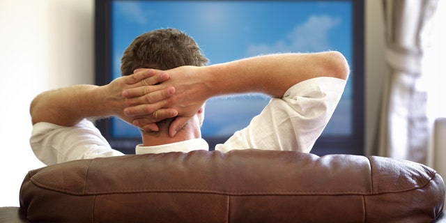 Man sitting on a sofa watching tv with hands folded behind his headPlease see similar picture from my portfolio: