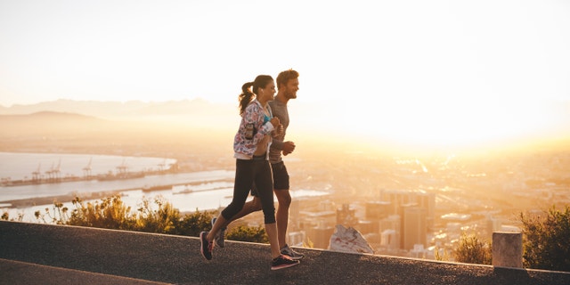 Shot of young couple running on hillside road outside the city. Young man and woman jogging in morning with bright sunlight.