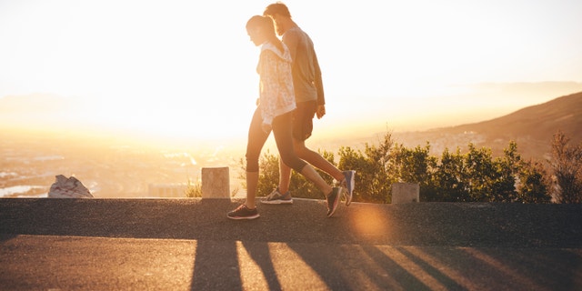 A couple takes a walk outside in bright sunlight. "Get sunlight as soon as you wake up and throughout the day to help you keep your melatonin levels in sync with your circadian rhythm."