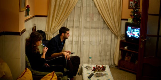 VILLACANAS, SPAIN - NOVEMBER 29: Unemployed twenty-year old Maria Regina Fernandez (L) spends the night watching television with her boyfriend, who does also not hold a job, instead of going out to the cinema or the villages bars and cafeterias, at their grandmothers home on November 29, 2012 in Villacanas, Spain. During the boom years, where in its peak Spain built some 800,000 houses a year accompanied by the manufacturing of millions of wooden doors, the people of Villacanas were part of Spain's middle class enjoying high wages and permanent jobs. During the construction boom years the majority of the doors used within these new developments were made in this small industrial town. Approximately seven million doors a year were once assembled here and the factory employed a workforce of almost 5700 people, but the town is now left almost desolate with the Villacanas industrial park now empty and redundant. With Spain in the grip of recession and the housing bubble burst, Villacanas is typical of many former buoyant industrial Spanish towns now struggling with huge unemployment problems. (Photo by Jasper Juinen/Getty Images)