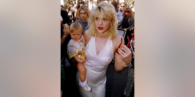 Kurt Cobain (L, behind baby), is shown as he arrives with wife Courtney Love, holding their daughter Frances Bean Cobain, for the MTV Music Awards in September 1992 in Los Angeles, Calif.