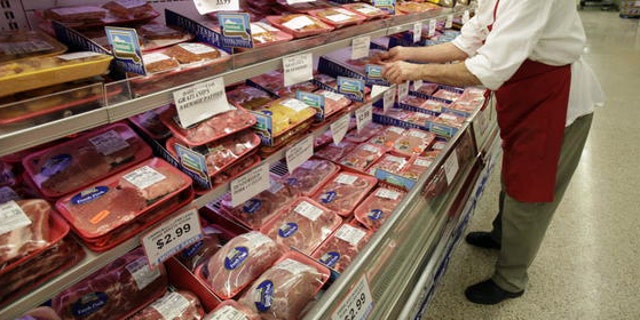 A butcher looks at several cuts of meat at a grocery store.