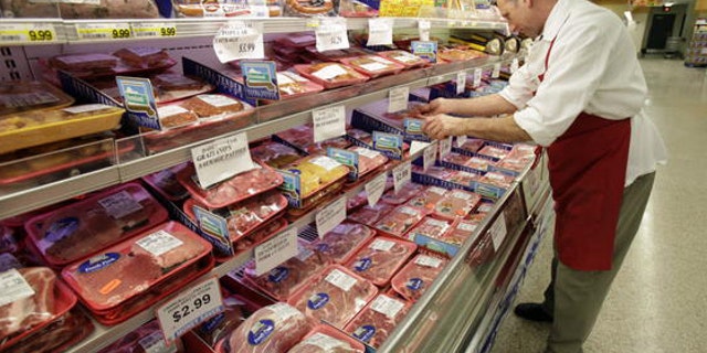 A butcher looks at several cuts of meat at a grocery store.
