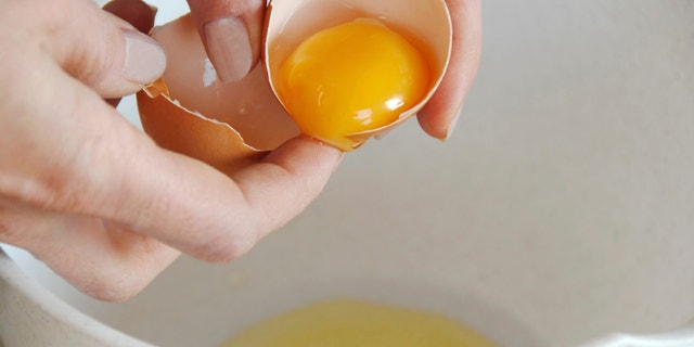 broken egg in hands with separated yolk closeup