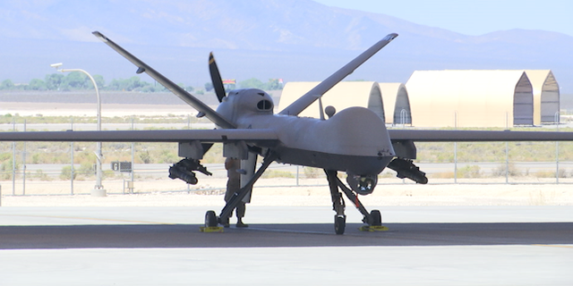 An MQ-9 Reaper drone is parked underneath a hangar on the tarmac at Creech Air Force Base.